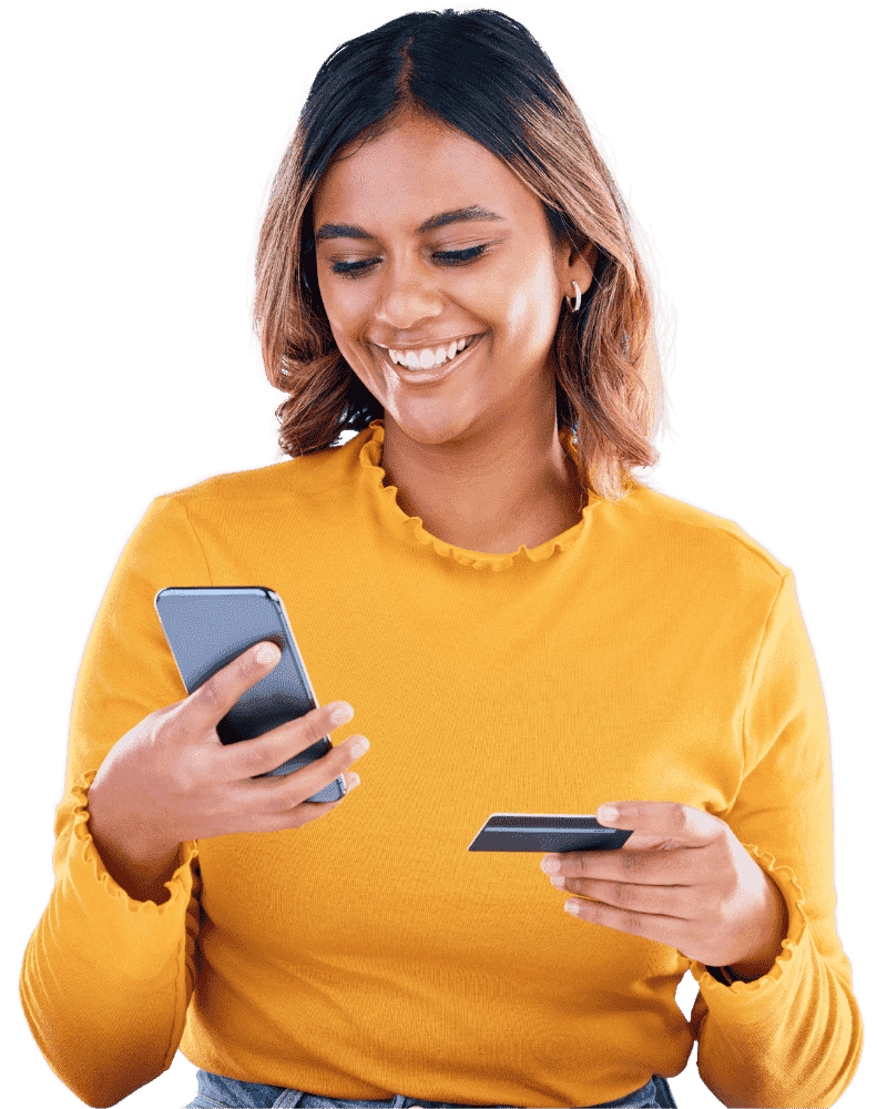 A smiling woman in a yellow sweater is holding a smartphone in one hand and a credit card in the other, looking pleased as she engages in a transaction.